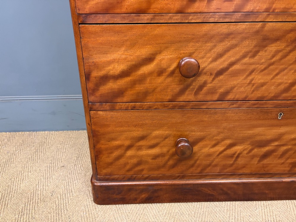 A Victorian chest of drawers in warm brown figured timber featuring turned handles and a plinth base. View IX