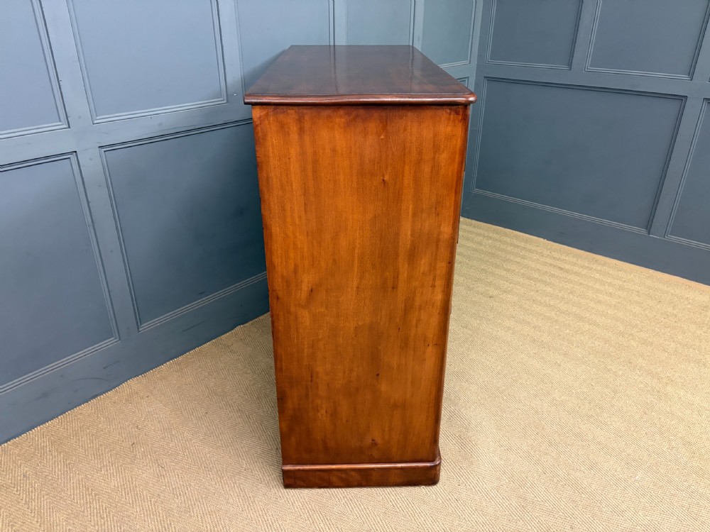 A Victorian chest of drawers in warm brown figured timber featuring turned handles and a plinth base. View XI