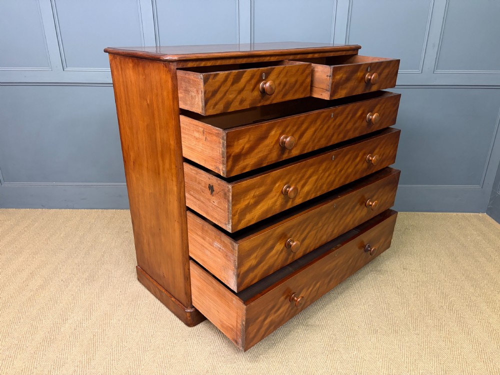 A Victorian chest of drawers in warm brown figured timber featuring turned handles and a plinth base. View XII