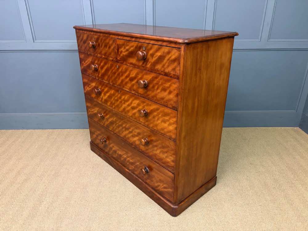 A Victorian chest of drawers in warm brown figured timber featuring turned handles and a plinth base. View XIII