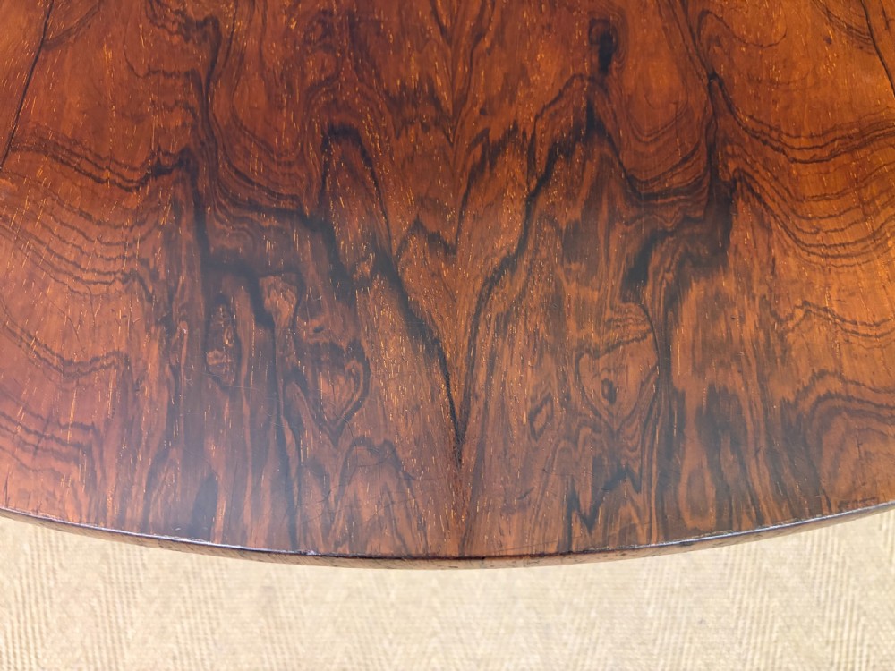 A Victorian oval rosewood loo table featuring a bookmatched veneer tabletop supported by a carved pedestal base with four scroll feet. View V