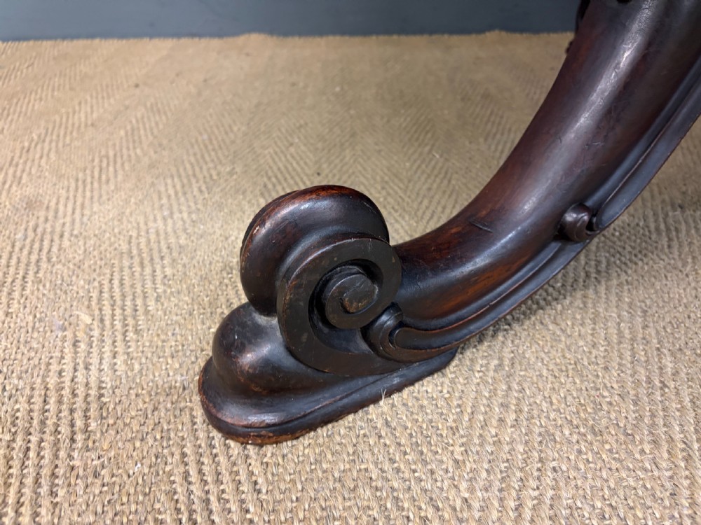 A Victorian oval rosewood loo table featuring a bookmatched veneer tabletop supported by a carved pedestal base with four scroll feet. View VIII