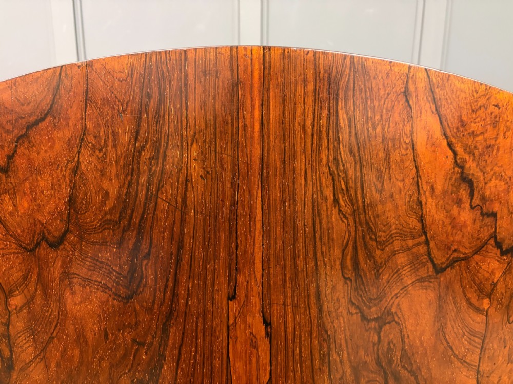 A Victorian oval rosewood loo table featuring a bookmatched veneer tabletop supported by a carved pedestal base with four scroll feet. View XIV