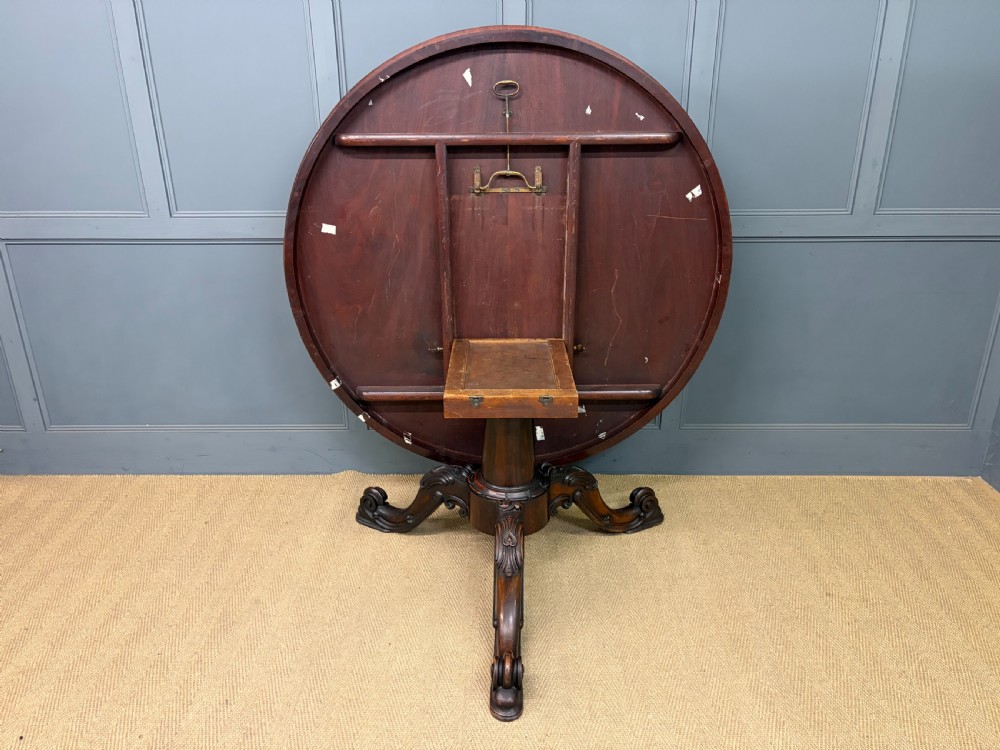 A Victorian oval rosewood loo table featuring a bookmatched veneer tabletop supported by a carved pedestal base with four scroll feet. View XVII