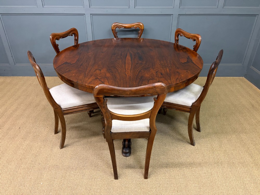 A Victorian oval rosewood loo table featuring a bookmatched veneer tabletop supported by a carved pedestal base with four scroll feet. View XXII
