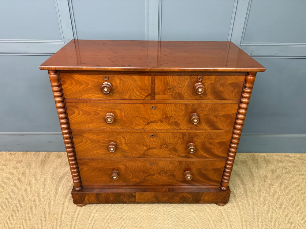 A Victorian flame mahogany chest of drawers featuring two short over three long drawers flanked by spiral turned columns resting on a solid plinth base. View II