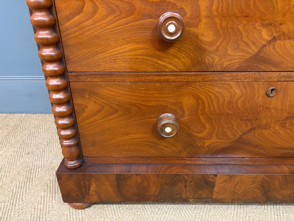 A Victorian flame mahogany chest of drawers featuring two short over three long drawers flanked by spiral turned columns resting on a solid plinth base. View VIII