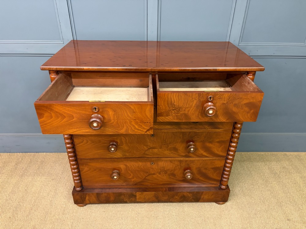 A Victorian flame mahogany chest of drawers featuring two short over three long drawers flanked by spiral turned columns resting on a solid plinth base. View IX