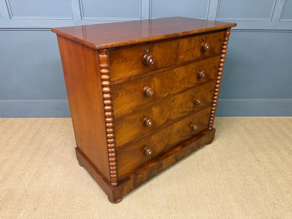 A Victorian flame mahogany chest of drawers featuring two short over three long drawers flanked by spiral turned columns resting on a solid plinth base. View X