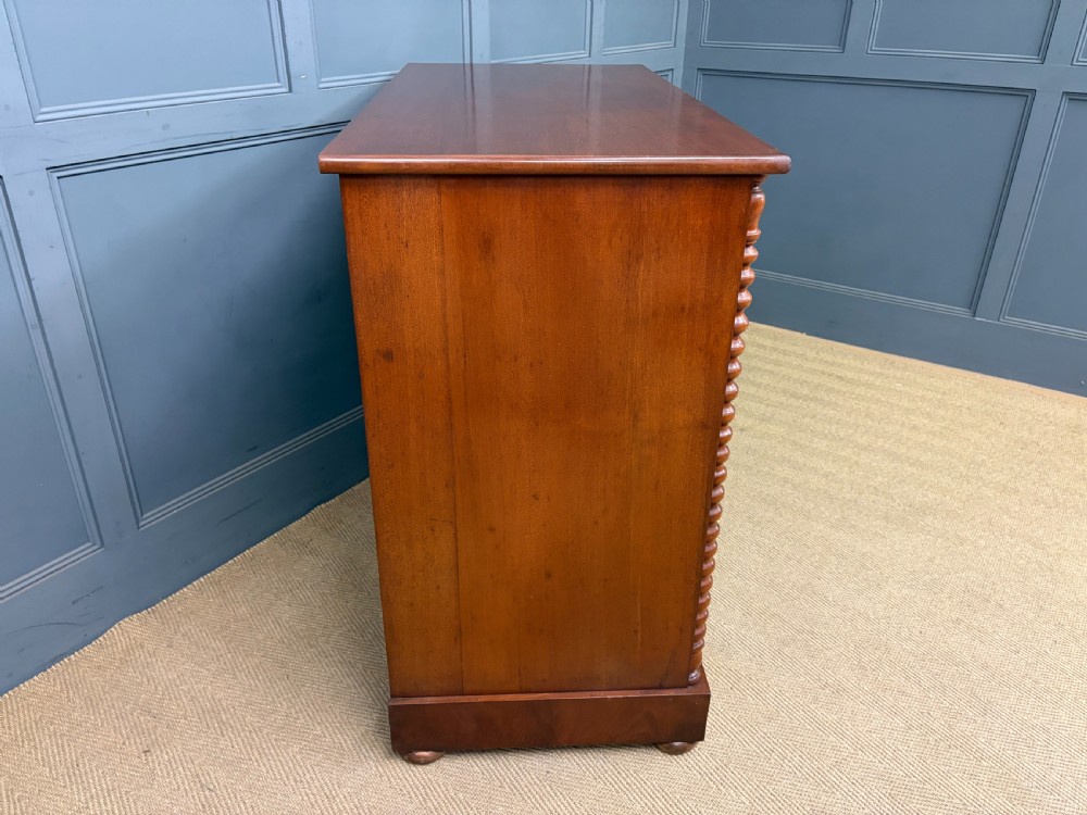 A Victorian flame mahogany chest of drawers featuring two short over three long drawers flanked by spiral turned columns resting on a solid plinth base. View XII