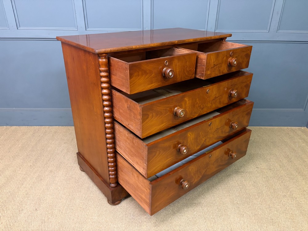 A Victorian flame mahogany chest of drawers featuring two short over three long drawers flanked by spiral turned columns resting on a solid plinth base. View XIII