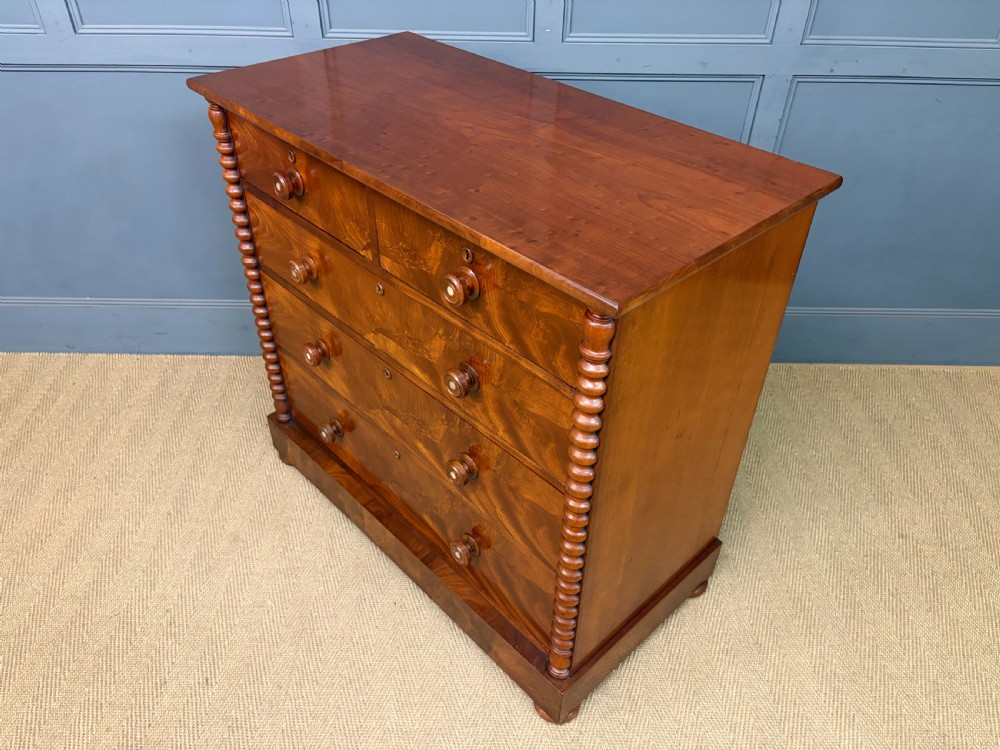 A Victorian flame mahogany chest of drawers featuring two short over three long drawers flanked by spiral turned columns resting on a solid plinth base. View XIV