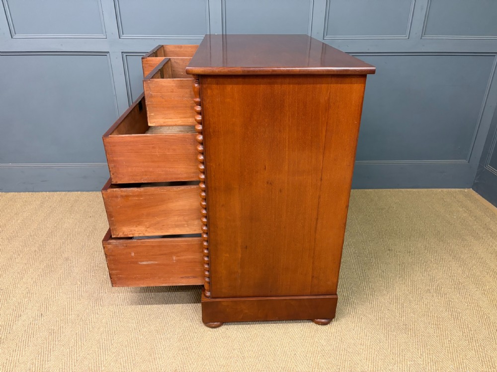 A Victorian flame mahogany chest of drawers featuring two short over three long drawers flanked by spiral turned columns resting on a solid plinth base. View XV