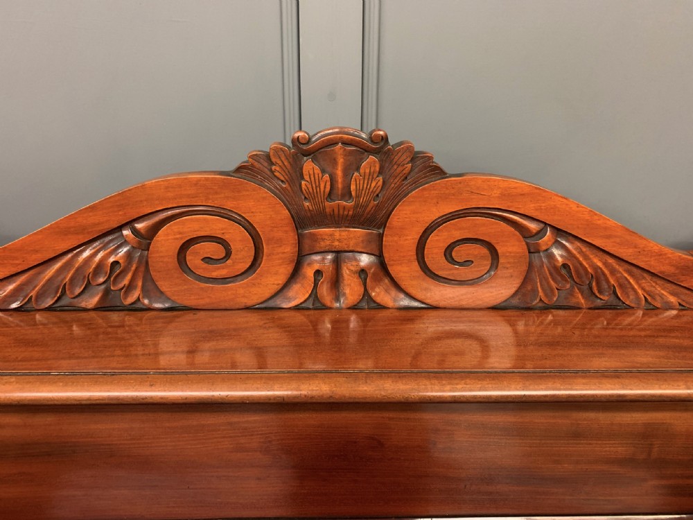 An early nineteenth-century flame mahogany chiffonier featuring a carved ornamental cresting, open central bookshelves, and two side cupboards. View V