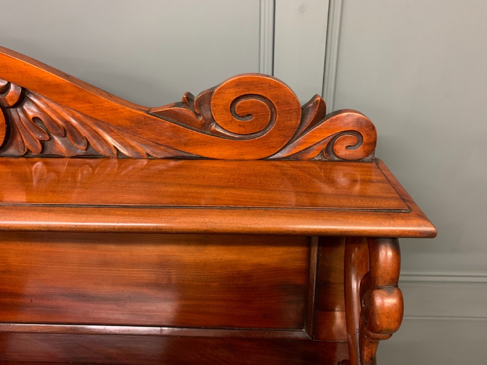An early nineteenth-century flame mahogany chiffonier featuring a carved ornamental cresting, open central bookshelves, and two side cupboards. View VI