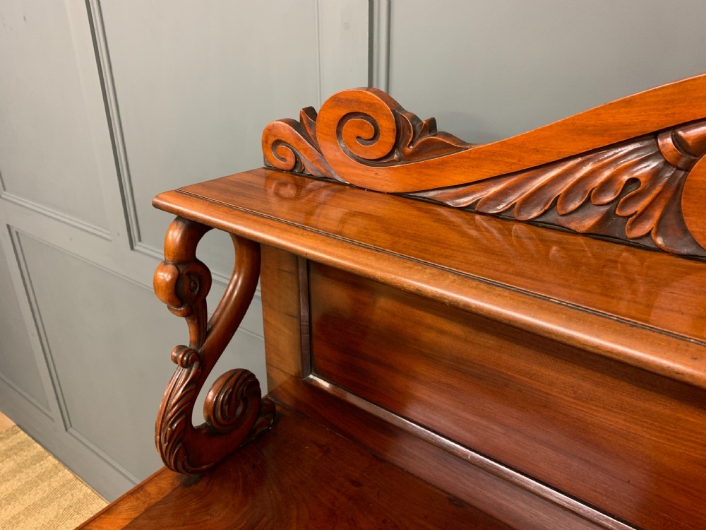 An early nineteenth-century flame mahogany chiffonier featuring a carved ornamental cresting, open central bookshelves, and two side cupboards. View VII