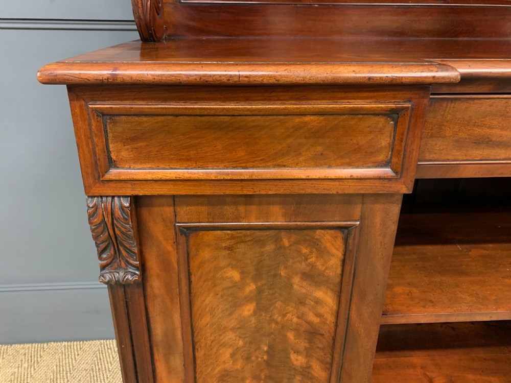 An early nineteenth-century flame mahogany chiffonier featuring a carved ornamental cresting, open central bookshelves, and two side cupboards. View X
