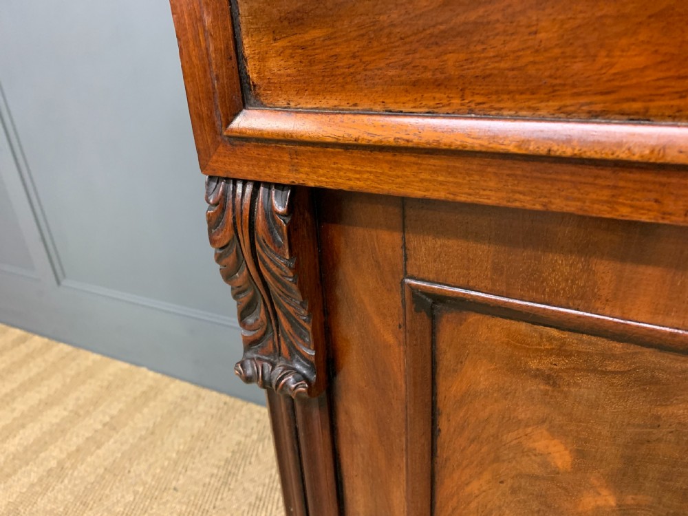 An early nineteenth-century flame mahogany chiffonier featuring a carved ornamental cresting, open central bookshelves, and two side cupboards. View XI