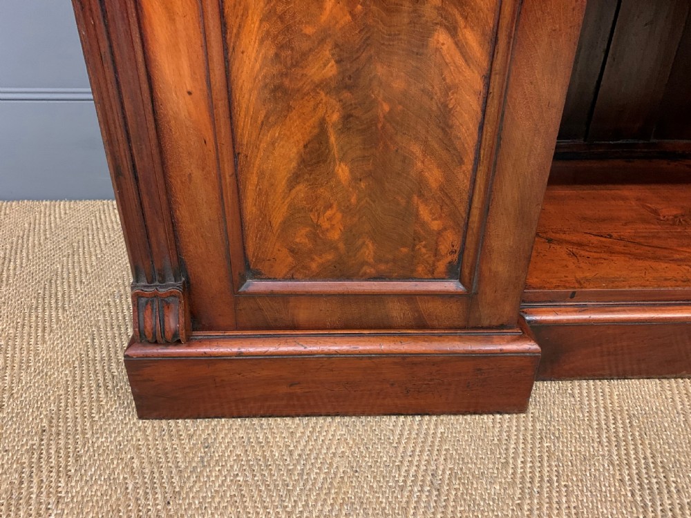 An early nineteenth-century flame mahogany chiffonier featuring a carved ornamental cresting, open central bookshelves, and two side cupboards. View XII