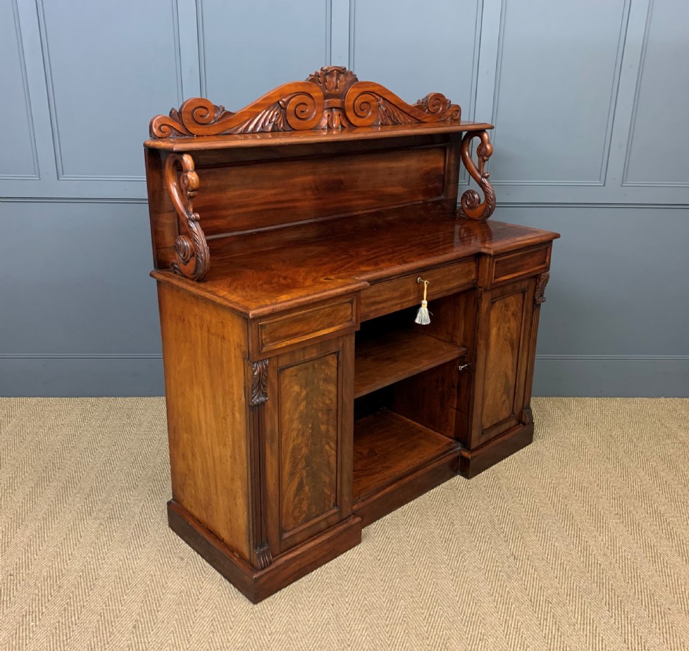 An early nineteenth-century flame mahogany chiffonier featuring a carved ornamental cresting, open central bookshelves, and two side cupboards. View XIV