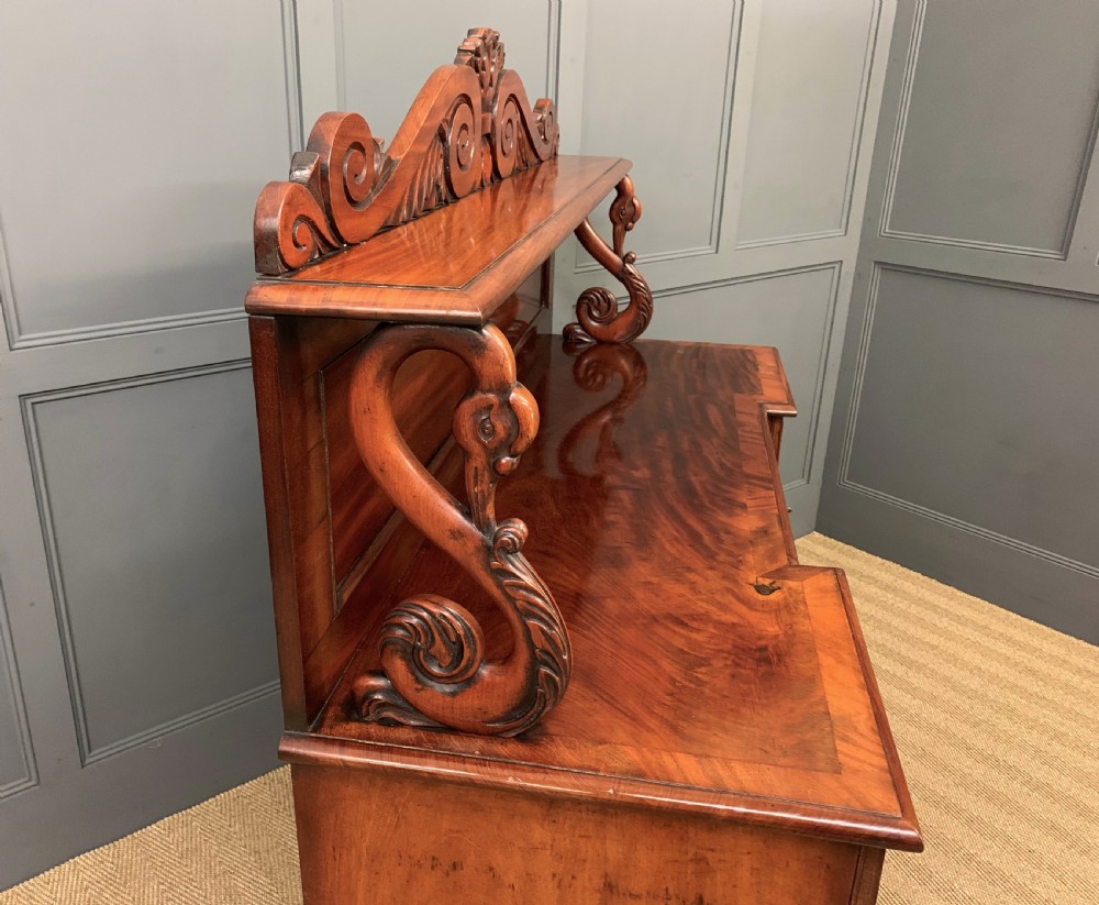An early nineteenth-century flame mahogany chiffonier featuring a carved ornamental cresting, open central bookshelves, and two side cupboards. View XVI