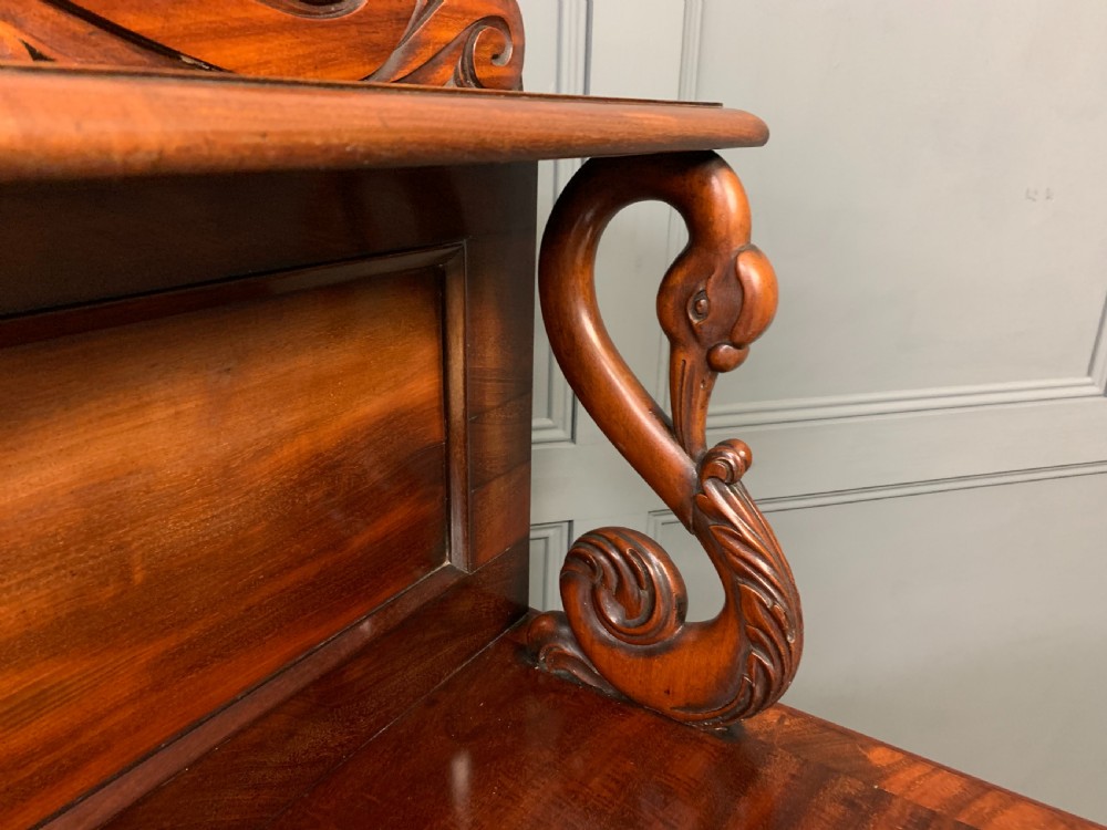 An early nineteenth-century flame mahogany chiffonier featuring a carved ornamental cresting, open central bookshelves, and two side cupboards. View XVII