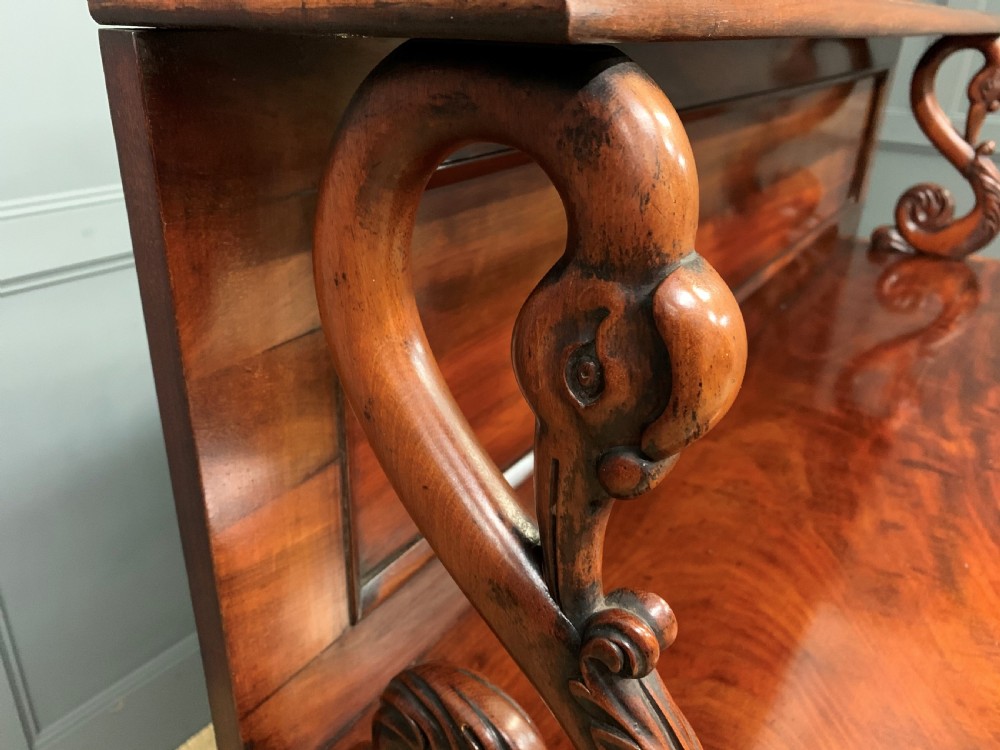 An early nineteenth-century flame mahogany chiffonier featuring a carved ornamental cresting, open central bookshelves, and two side cupboards. View XXII