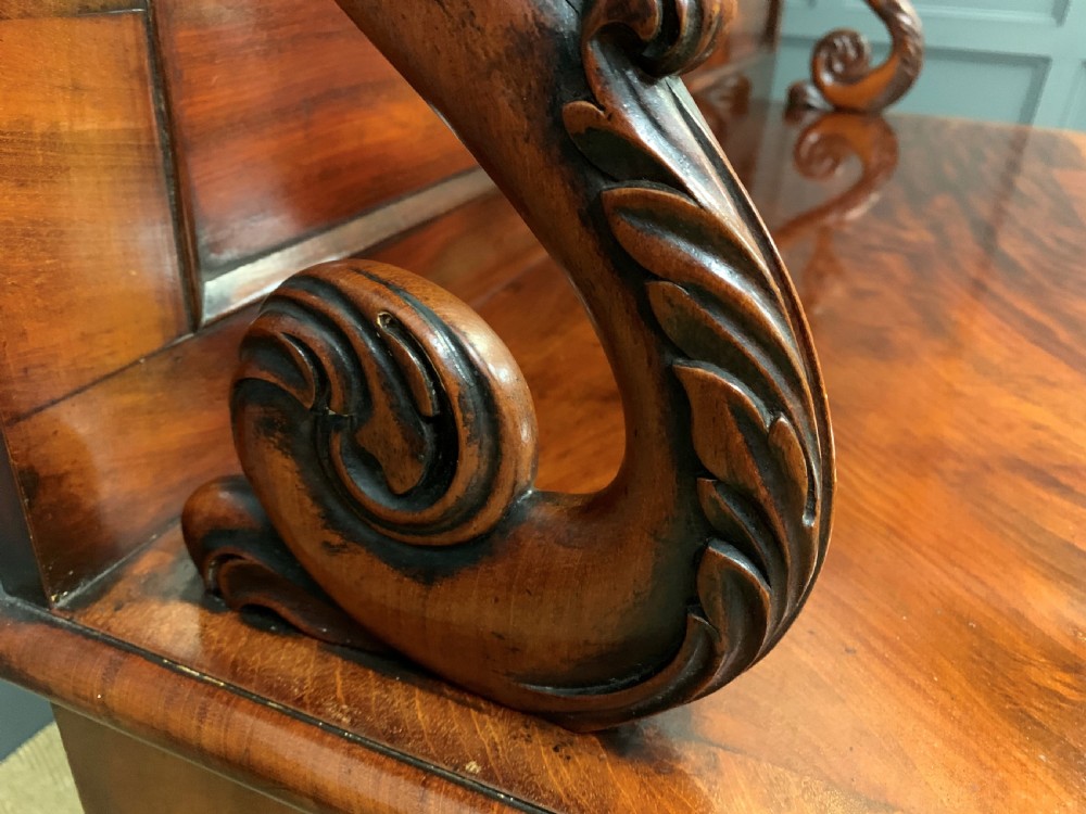 An early nineteenth-century flame mahogany chiffonier featuring a carved ornamental cresting, open central bookshelves, and two side cupboards. View XXIII