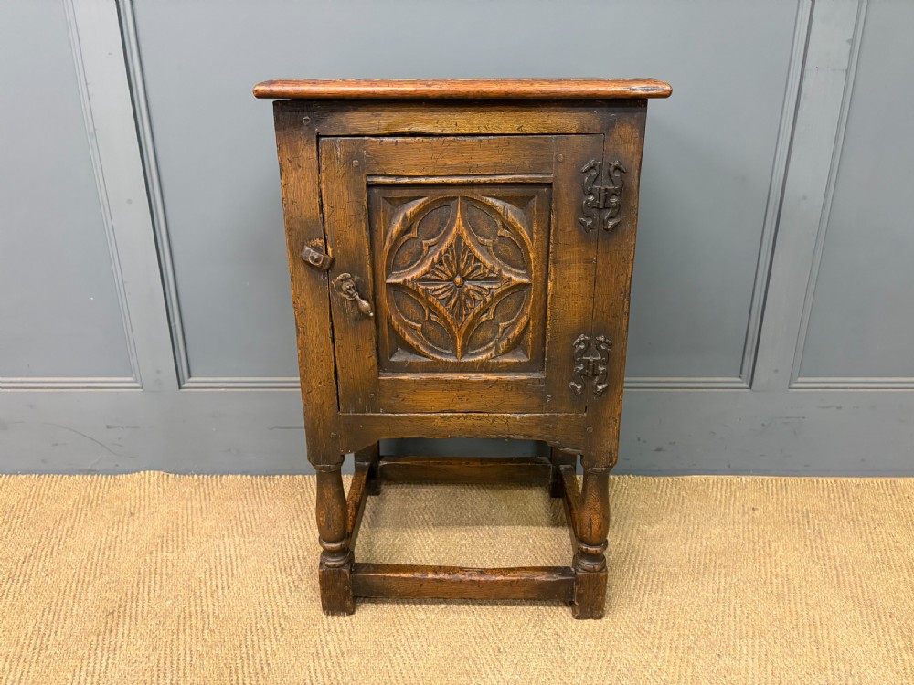 A small dark brown oak cupboard featuring a carved medallion door panel, wrought iron hardware, and turned legs. View II