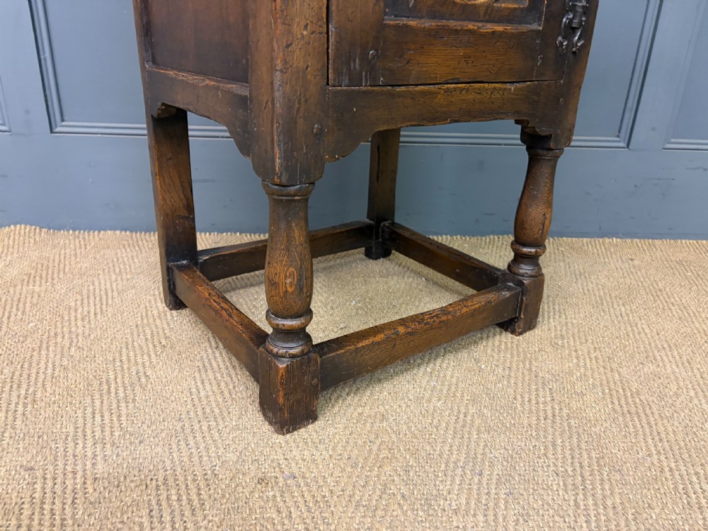 A small dark brown oak cupboard featuring a carved medallion door panel, wrought iron hardware, and turned legs. View VIII