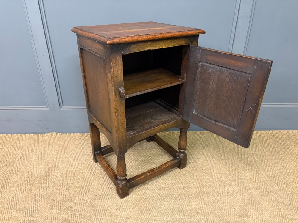 A small dark brown oak cupboard featuring a carved medallion door panel, wrought iron hardware, and turned legs. View IX