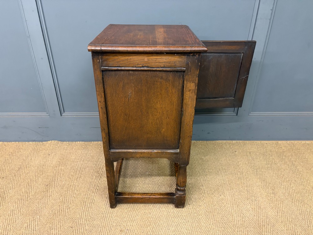 A small dark brown oak cupboard featuring a carved medallion door panel, wrought iron hardware, and turned legs. View X