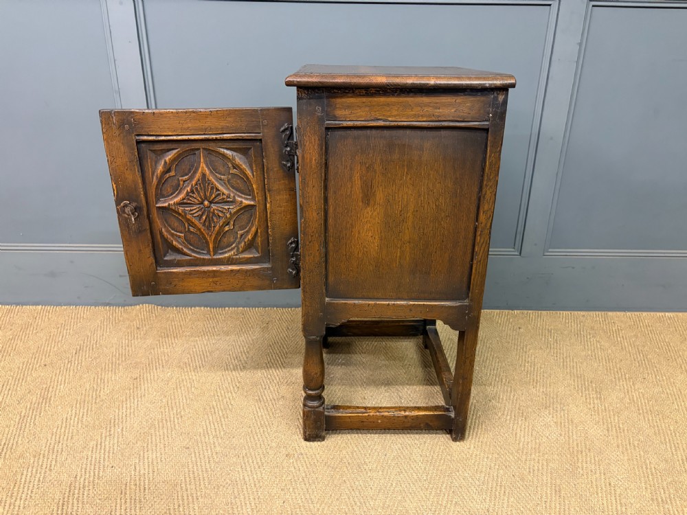 A small dark brown oak cupboard featuring a carved medallion door panel, wrought iron hardware, and turned legs. View XI