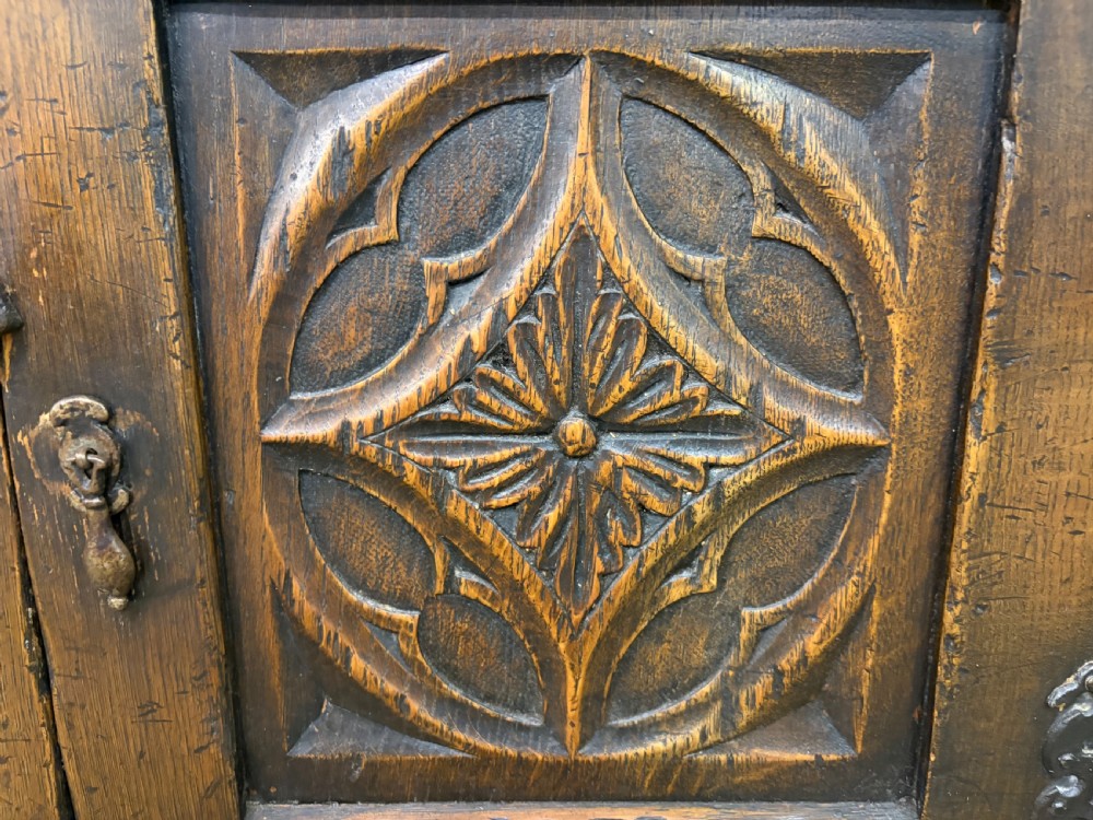 A small dark brown oak cupboard featuring a carved medallion door panel, wrought iron hardware, and turned legs. View XII