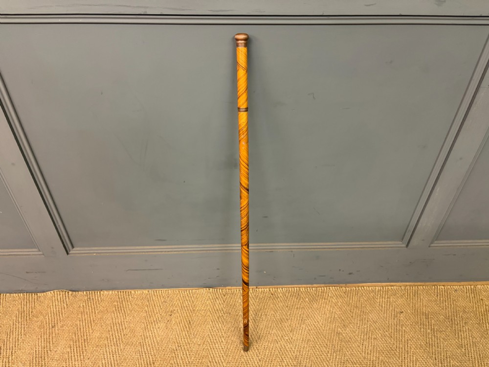 A Victorian wooden walking cane featuring a spiral pattern along the tapered shaft and a metal collar.
