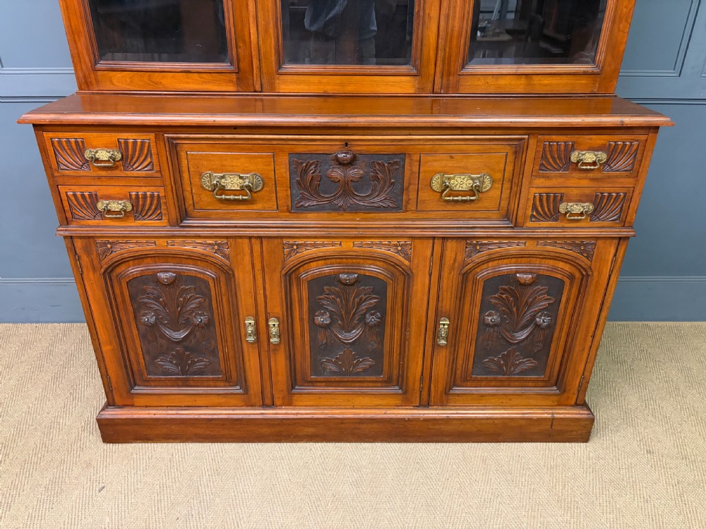 A large Victorian walnut secretaire bookcase featuring three upper glazed doors with arched panels over a central carved writing drawer and lower carved cupboard doors. View IV