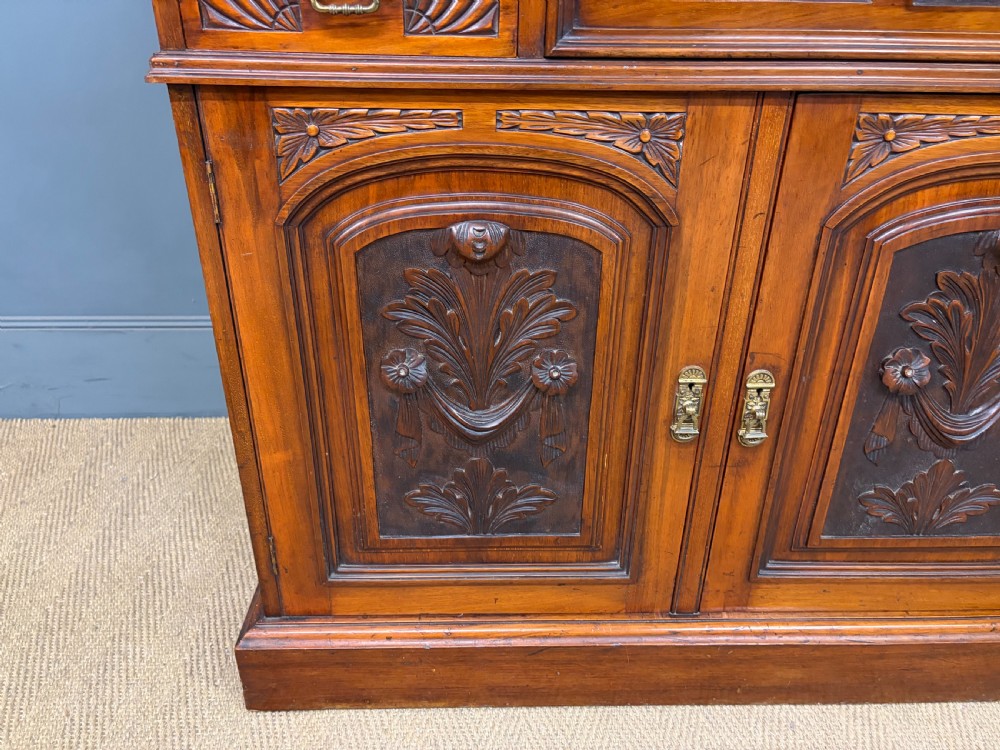 A large Victorian walnut secretaire bookcase featuring three upper glazed doors with arched panels over a central carved writing drawer and lower carved cupboard doors. View VIII