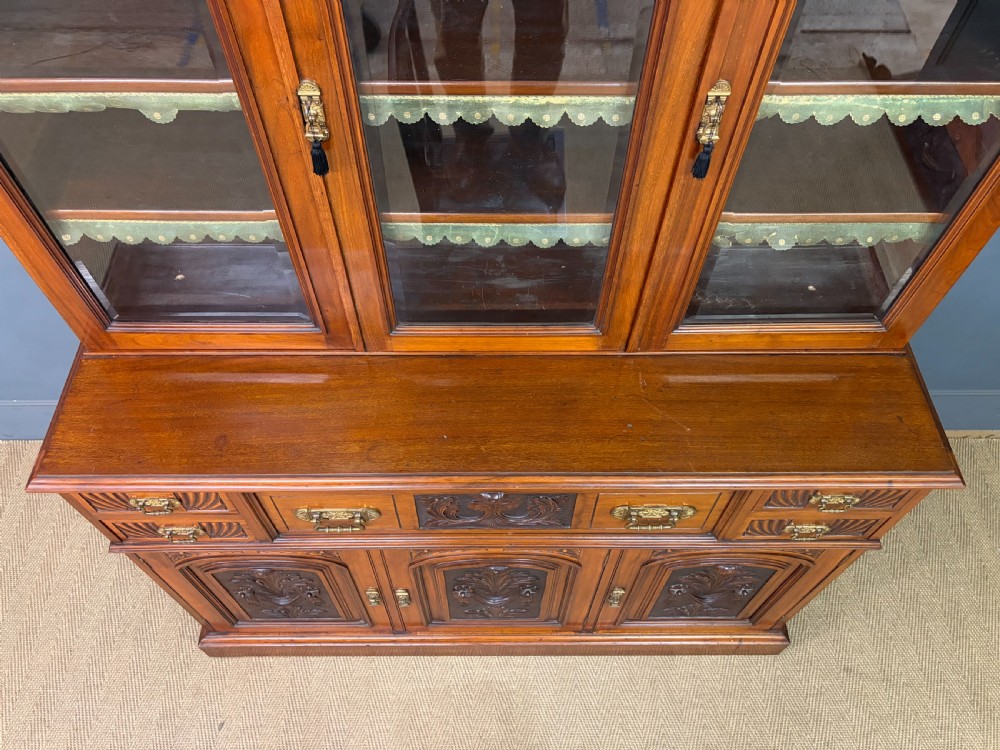 A large Victorian walnut secretaire bookcase featuring three upper glazed doors with arched panels over a central carved writing drawer and lower carved cupboard doors. View X