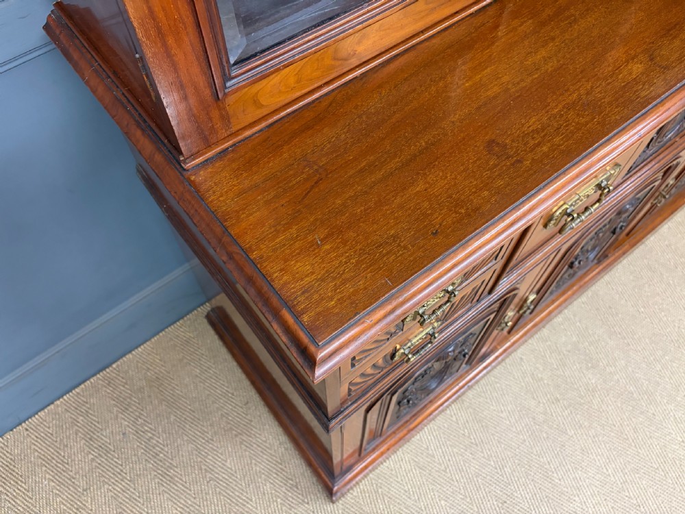 A large Victorian walnut secretaire bookcase featuring three upper glazed doors with arched panels over a central carved writing drawer and lower carved cupboard doors. View XII