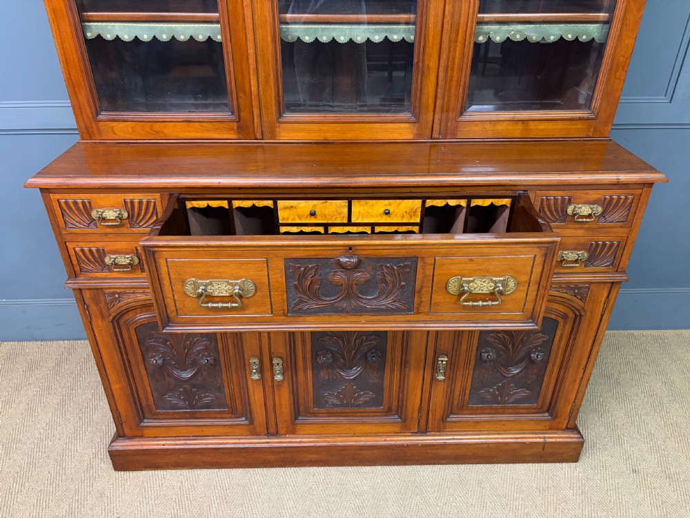 A large Victorian walnut secretaire bookcase featuring three upper glazed doors with arched panels over a central carved writing drawer and lower carved cupboard doors. View XVI
