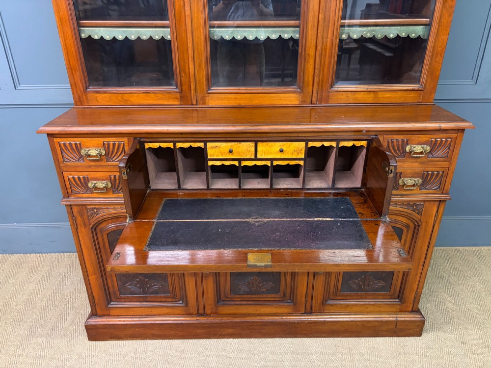 A large Victorian walnut secretaire bookcase featuring three upper glazed doors with arched panels over a central carved writing drawer and lower carved cupboard doors. View XVIII