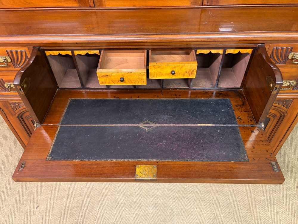 A large Victorian walnut secretaire bookcase featuring three upper glazed doors with arched panels over a central carved writing drawer and lower carved cupboard doors. View XIX