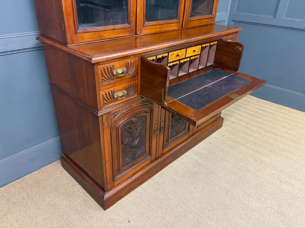 A large Victorian walnut secretaire bookcase featuring three upper glazed doors with arched panels over a central carved writing drawer and lower carved cupboard doors. View XX