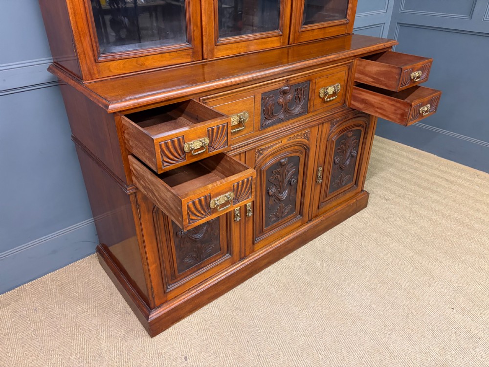 A large Victorian walnut secretaire bookcase featuring three upper glazed doors with arched panels over a central carved writing drawer and lower carved cupboard doors. View XXI