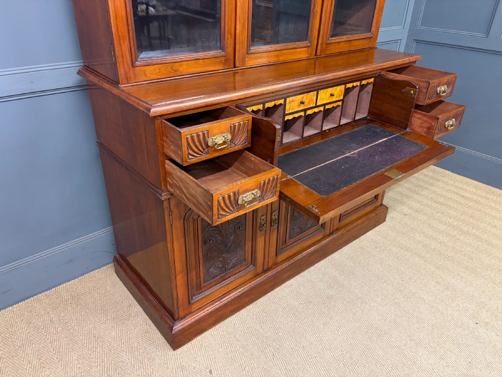 A large Victorian walnut secretaire bookcase featuring three upper glazed doors with arched panels over a central carved writing drawer and lower carved cupboard doors. View XXII