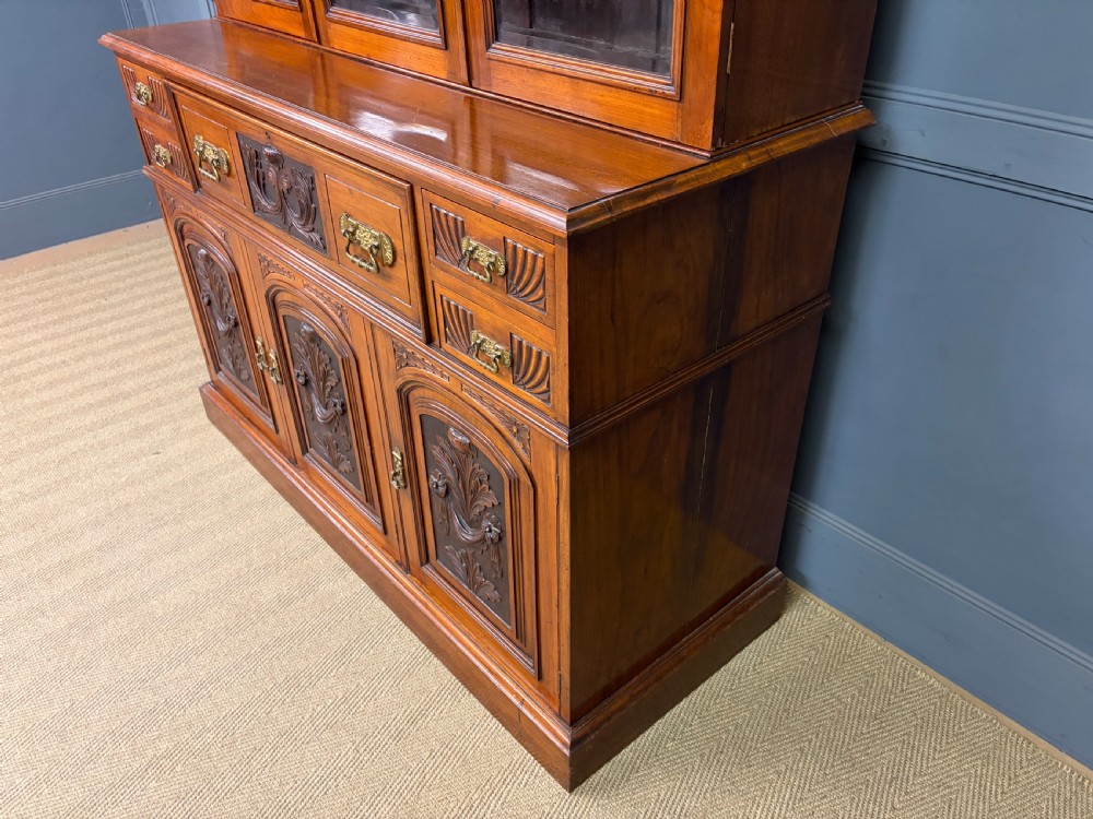 A large Victorian walnut secretaire bookcase featuring three upper glazed doors with arched panels over a central carved writing drawer and lower carved cupboard doors. View XXIV