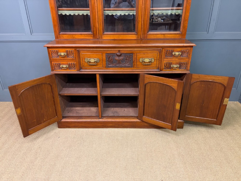 A large Victorian walnut secretaire bookcase featuring three upper glazed doors with arched panels over a central carved writing drawer and lower carved cupboard doors. View XXV