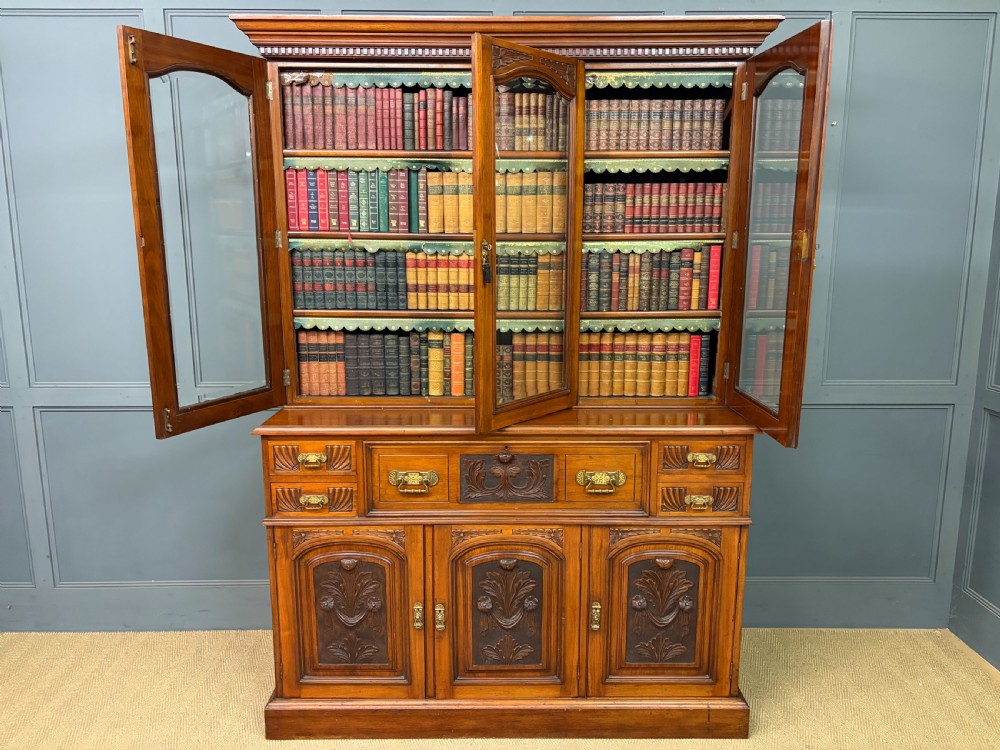 A large Victorian walnut secretaire bookcase featuring three upper glazed doors with arched panels over a central carved writing drawer and lower carved cupboard doors. View XXIX