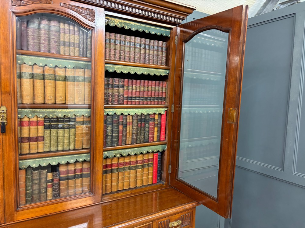 A large Victorian walnut secretaire bookcase featuring three upper glazed doors with arched panels over a central carved writing drawer and lower carved cupboard doors. View XXX