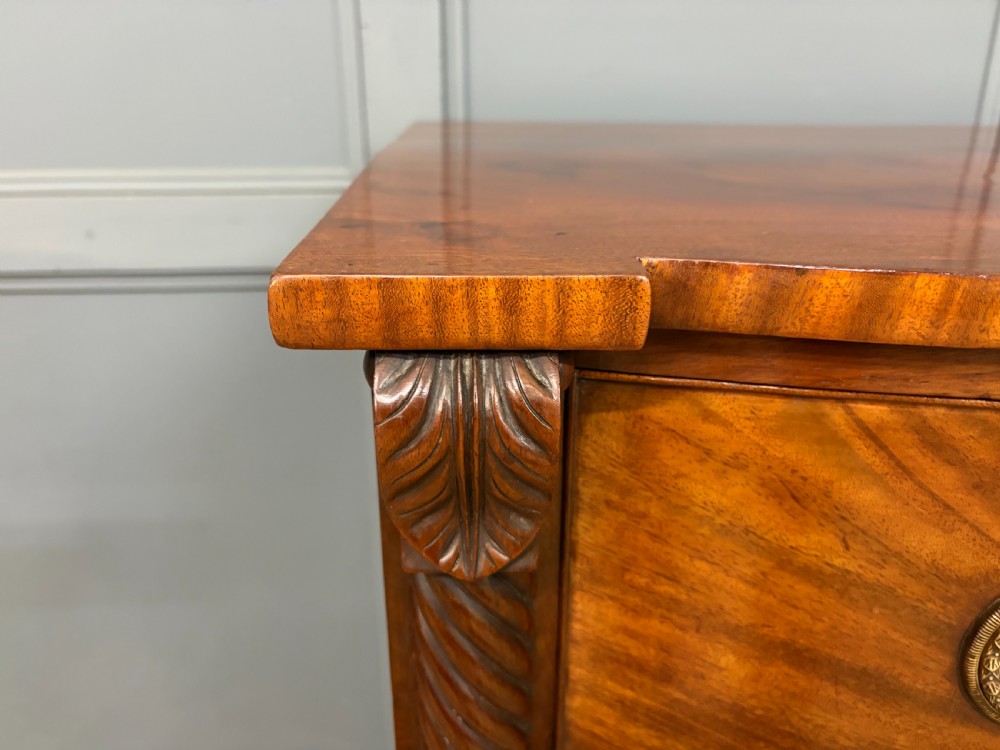 A Regency period mahogany bowfront chest of drawers featuring four graduated drawers, reeded side columns, brass ring handles, and turned feet. View VII